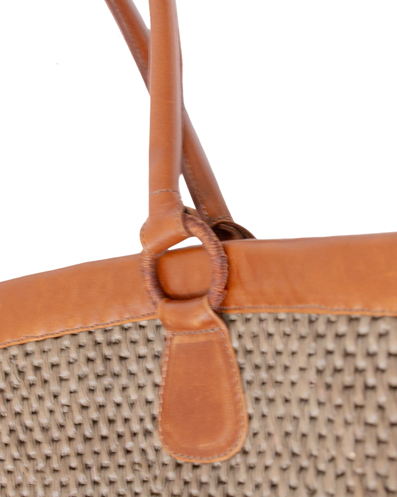 Mer Vert woven Ecuadorian straw tote bag with tan vachetta leather handles attached by circular rings.