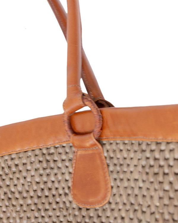 Mer Vert woven Ecuadorian straw tote bag with tan vachetta leather handles attached by circular rings.