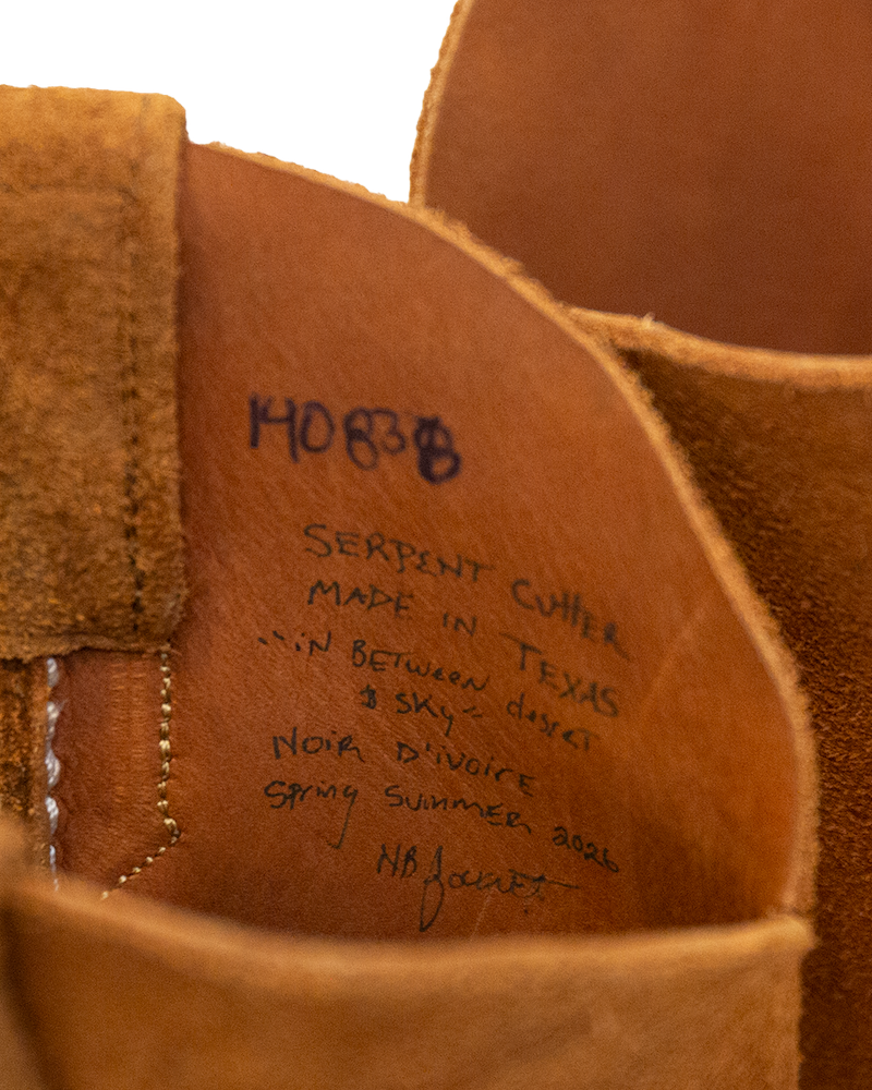 Interior detail of a whiskey brown suede Serpent Cutter boot featuring handwritten text: 14083B, Serpent Cutter, Made in Texas, In between desert & sky, Noir dIvoire, Spring Summer 2026, and a signature.