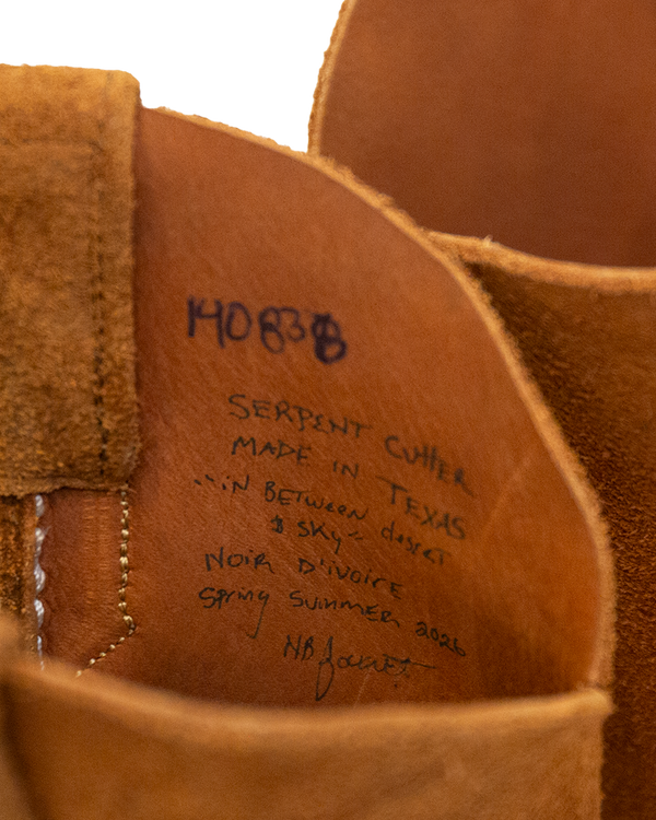 Interior detail of a whiskey brown suede Serpent Cutter boot featuring handwritten text: 14083B, Serpent Cutter, Made in Texas, In between desert & sky, Noir dIvoire, Spring Summer 2026, and a signature.