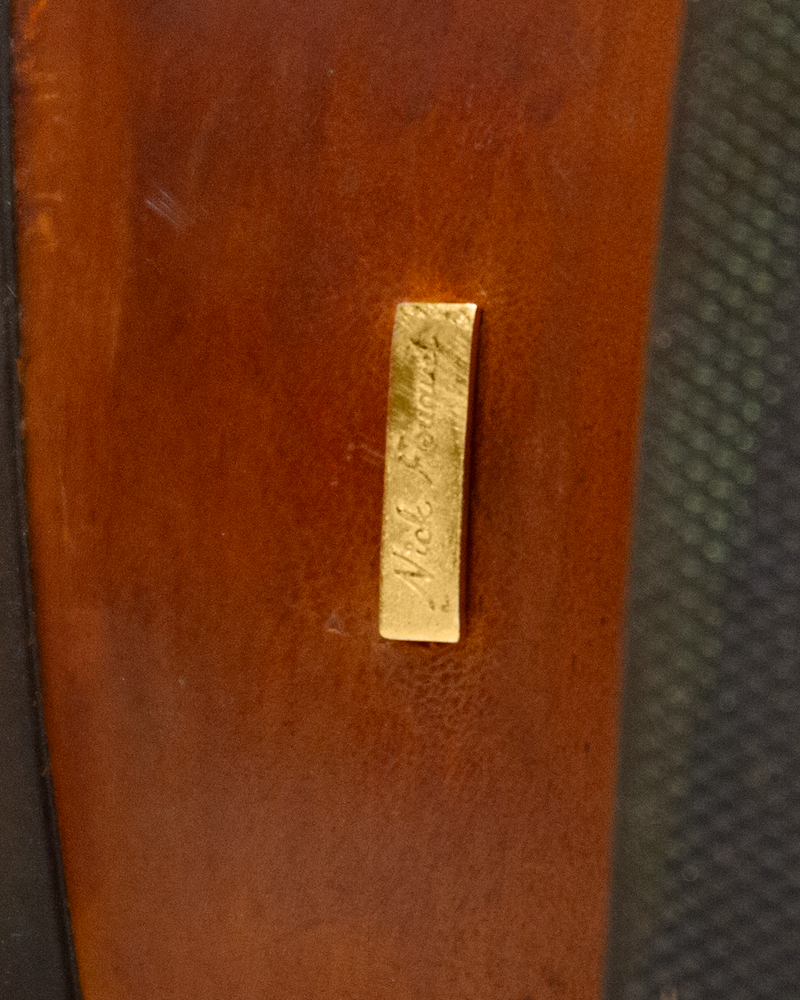 Close-up of a rectangular gold-toned metal tag engraved with the Silo Roper signature, attached to a smooth whiskey brown surface.