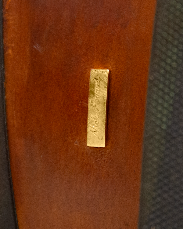 Close-up of a rectangular gold-toned metal tag engraved with the Silo Roper signature, attached to a smooth whiskey brown surface.