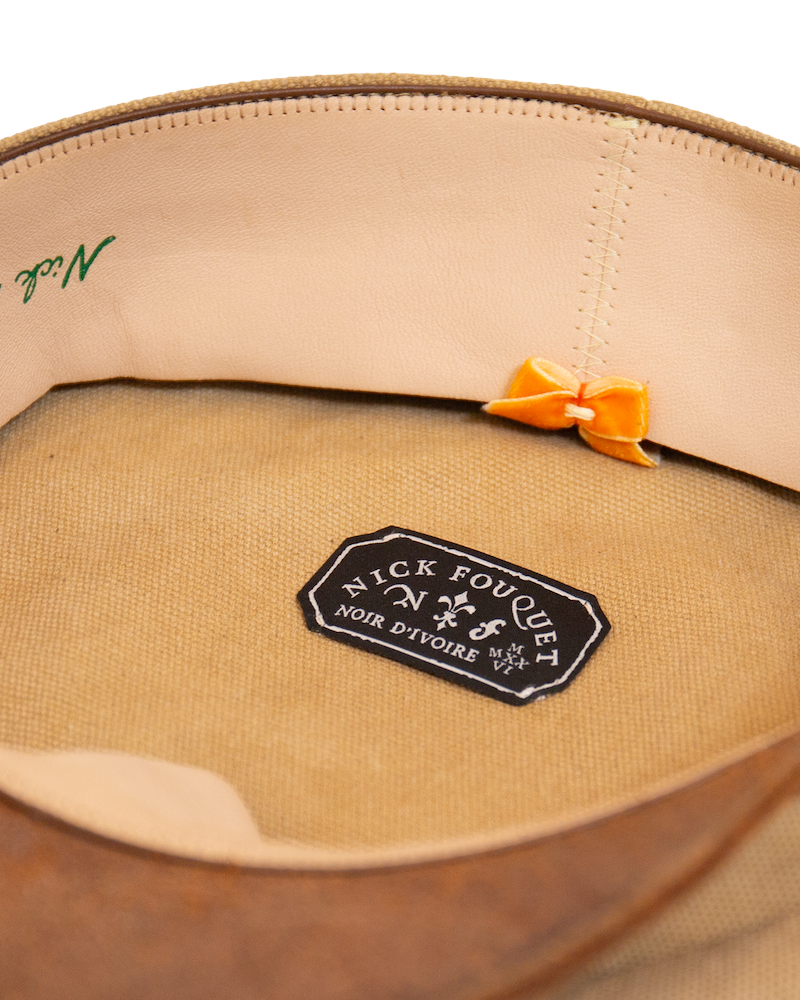 Inside view of the Alcyon canvas hat featuring a light-colored sweatband, a small orange bow, and a black rectangular brand label centered on the crown lining.