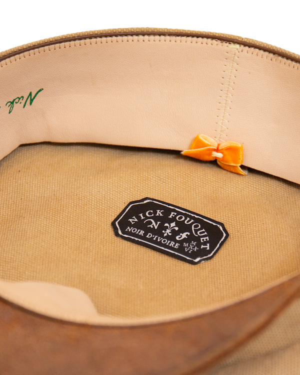 Inside view of the Alcyon canvas hat featuring a light-colored sweatband, a small orange bow, and a black rectangular brand label centered on the crown lining.