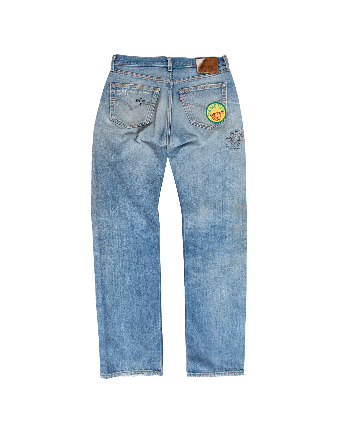 Back view of light-wash blue Rodeo Denim jeans, featuring a circular green and yellow patch on the right pocket, a small embroidered figure on the right leg, and handwritten-style text above the left pocket.